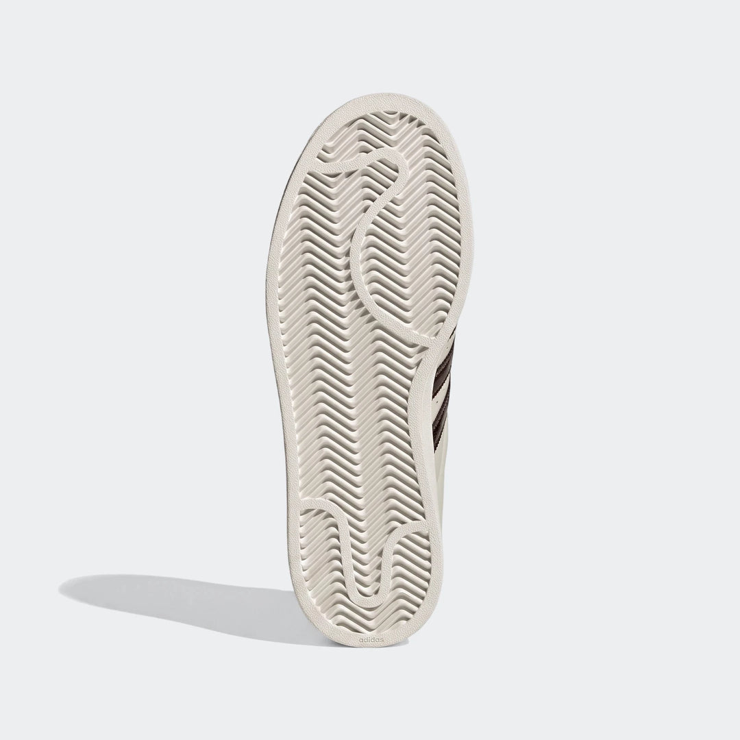 Bottom view of an Adidas Superstar II shoe sole in light cream, featuring a chevron-patterned tread and glimpses of brown