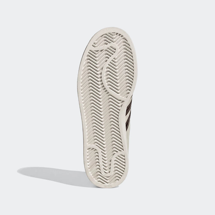 Bottom view of an Adidas Superstar II shoe sole in light cream, featuring a chevron-patterned tread and glimpses of brown