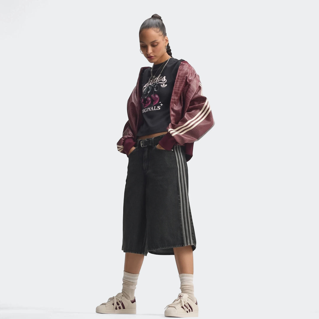 A female model showcasing Adidas Superstar II shoes with maroon stripes, dark denim shorts, and a maroon bomber jacket on a