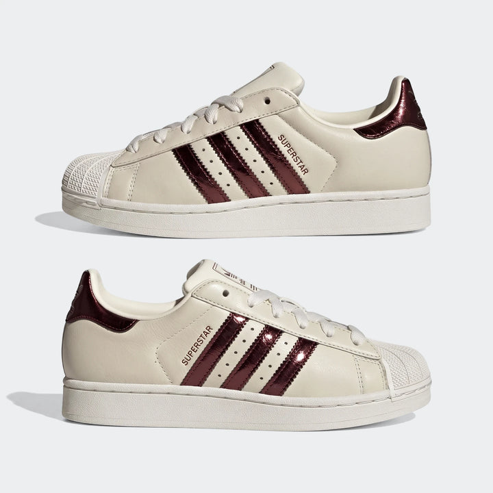 Two Adidas Superstar II shoes in off-white leather with metallic burgundy stripes and shell toes, angled view.