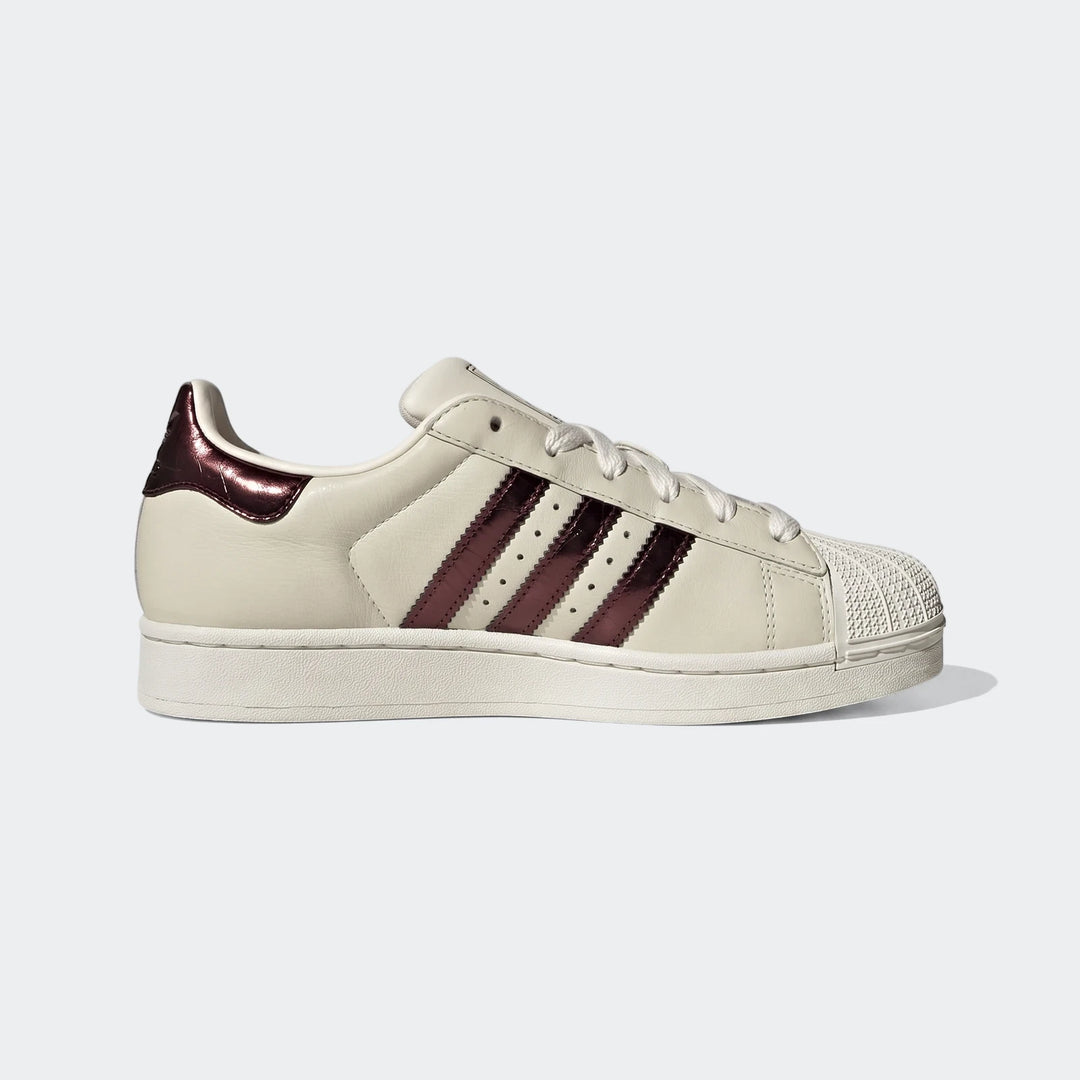 Off-white Adidas Superstar II shoes with metallic burgundy stripes, shown in a side profile view.