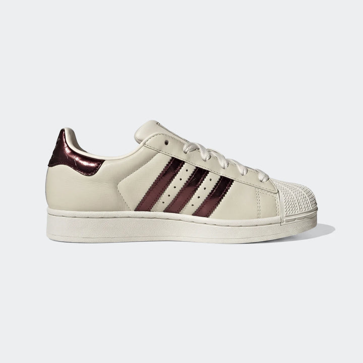 Off-white Adidas Superstar II shoes with metallic burgundy stripes, shown in a side profile view.