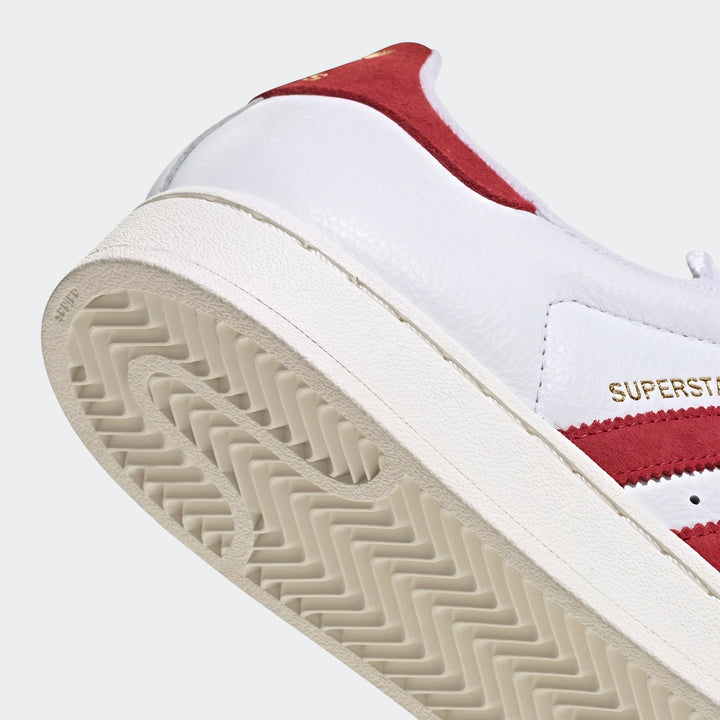 Close-up view of the heel and outsole of a white and red Adidas Superstar II shoe, showing the signature three stripes.