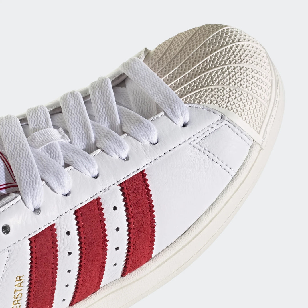 Close-up of a white leather Adidas Superstar II shoe featuring three vibrant red side stripes and white laces, showcasing