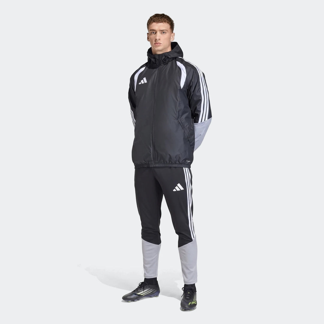 Male model wears an Adidas Tiro 26 Competition All-Weather Jacket and matching tracksuit in black and grey, studio shot.