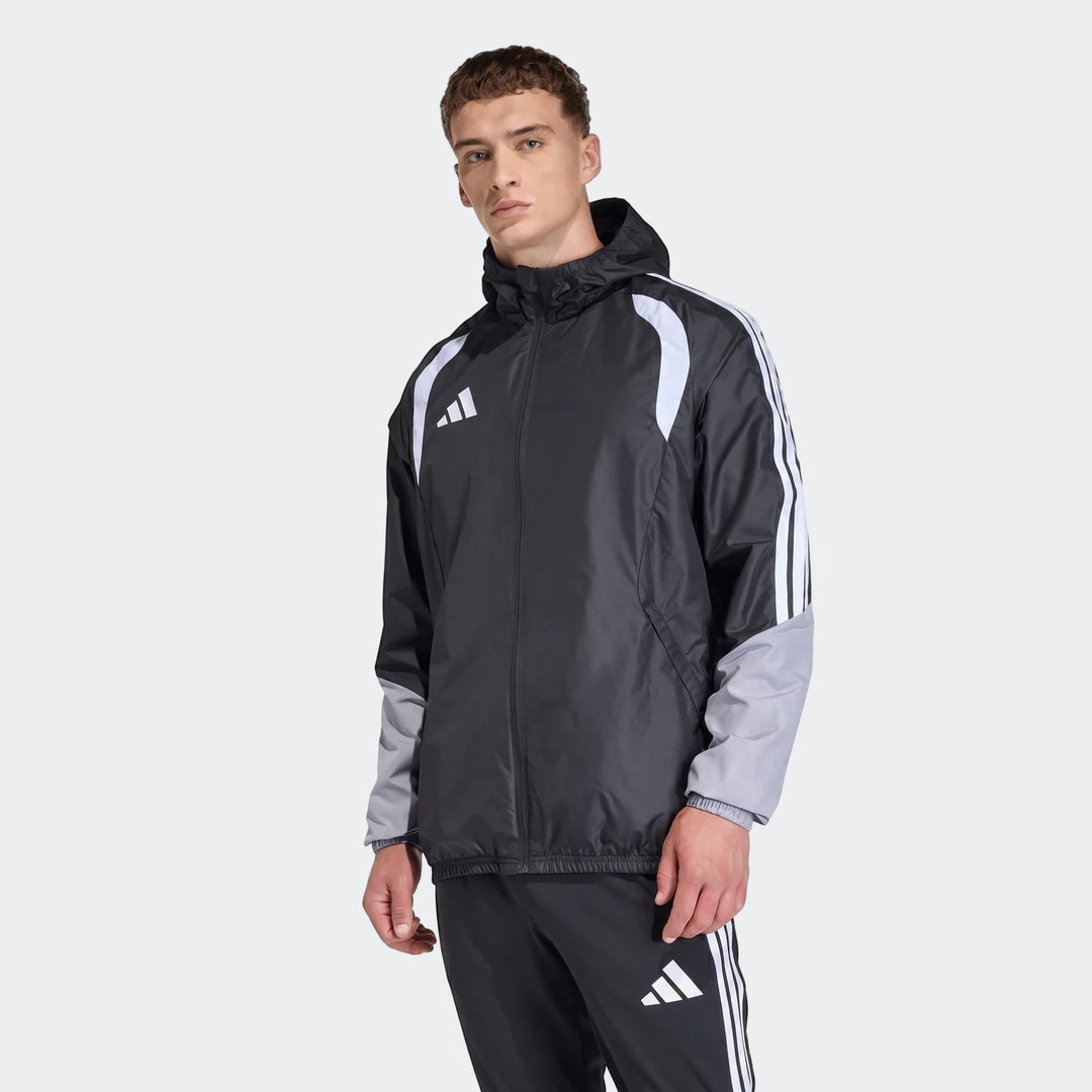 Male model wearing a black, white, and grey Adidas Tiro 26 Competition All-Weather Jacket and matching track pants, standing.