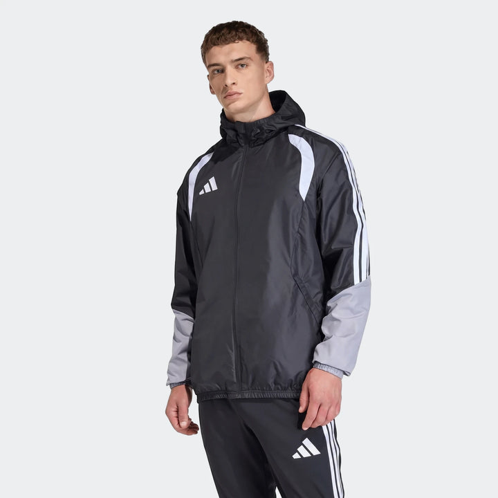 Male model wearing a black, white, and grey Adidas Tiro 26 Competition All-Weather Jacket and matching track pants, standing.