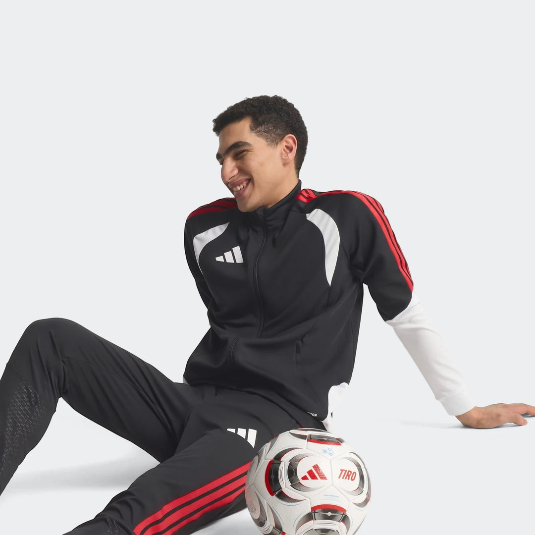 Male model wearing a black, red, and white Adidas Tiro 26 Competition Training Jacket and matching pants, with a soccer ball.