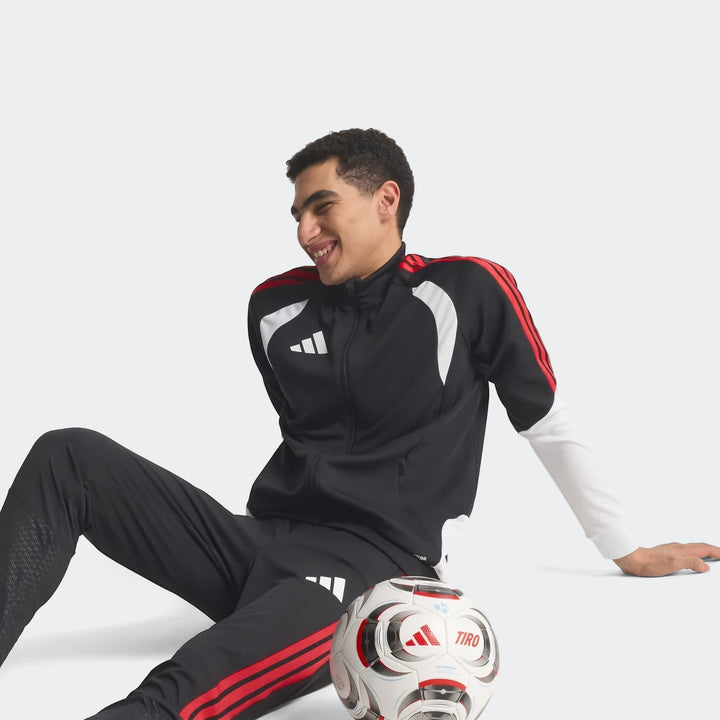 Male model wearing a black, red, and white Adidas Tiro 26 Competition Training Jacket and matching pants, with a soccer ball.
