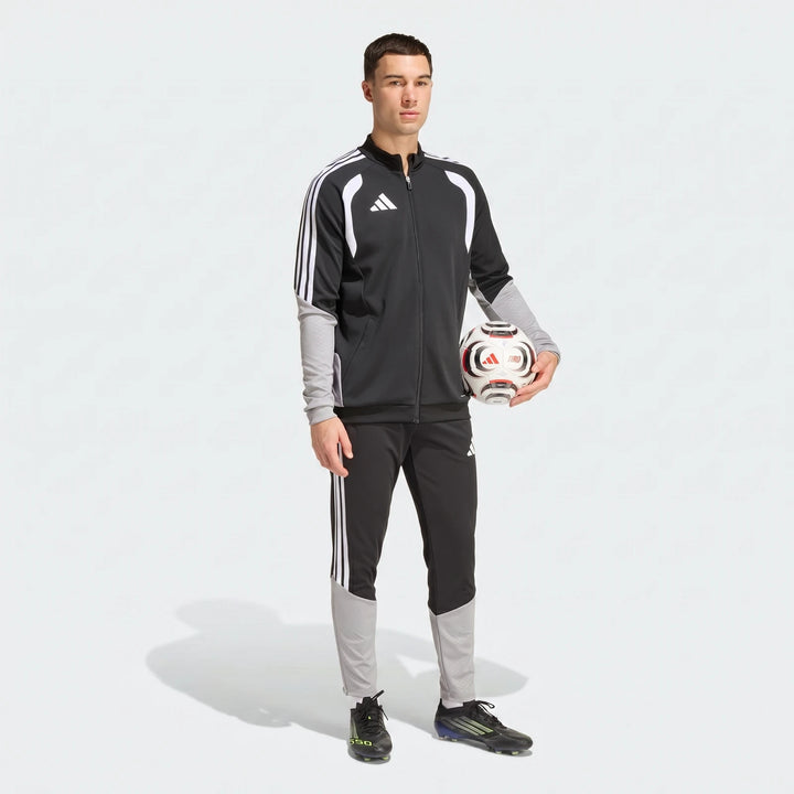 Male model wearing an Adidas Tiro 26 Competition Training Jacket and matching pants, holding a soccer ball, full body shot.