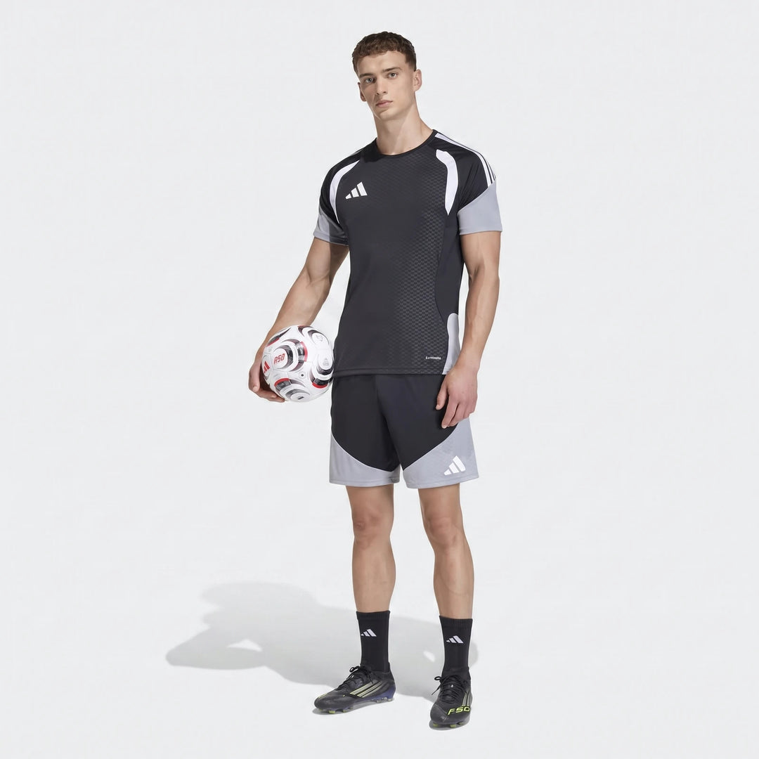 Male model wearing black and grey adidas Tiro 26 Competition Training Shorts and matching shirt, holding a soccer ball.