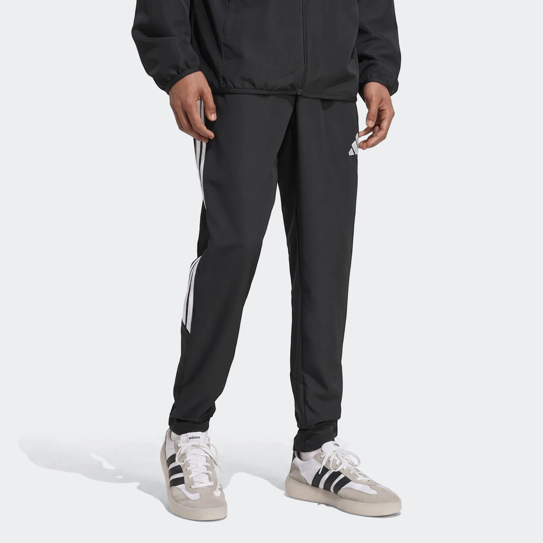 Black Adidas Tiro 26 League Presentation Pants modeled by a man, featuring iconic white three-stripes down the legs and