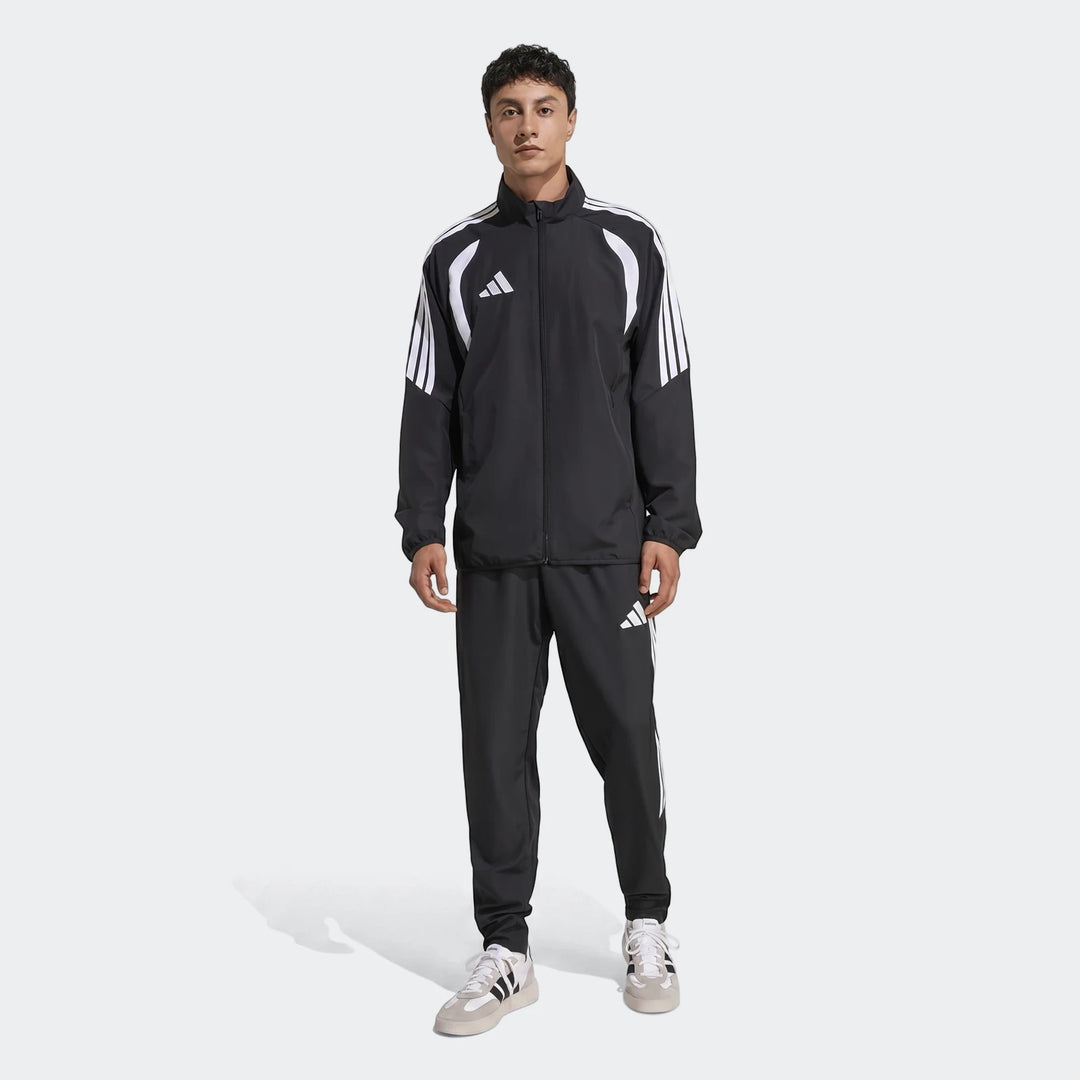 Full length shot of a man wearing a black Adidas Tiro 26 League Presentation tracksuit with white stripes and logos.