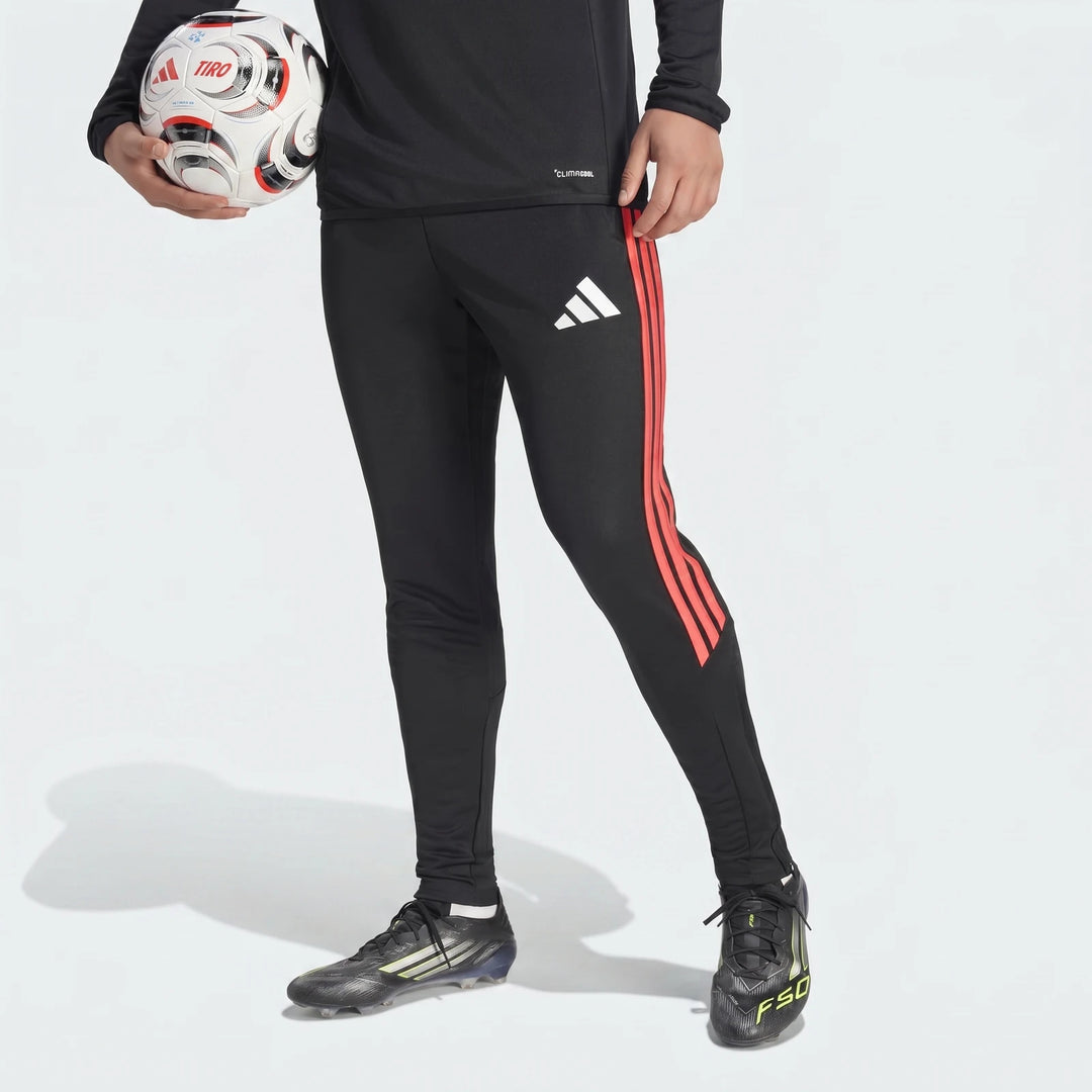 Black Adidas Tiro 26 League Training Tracksuit Bottoms with red stripes, worn by a person holding a soccer ball and wearing