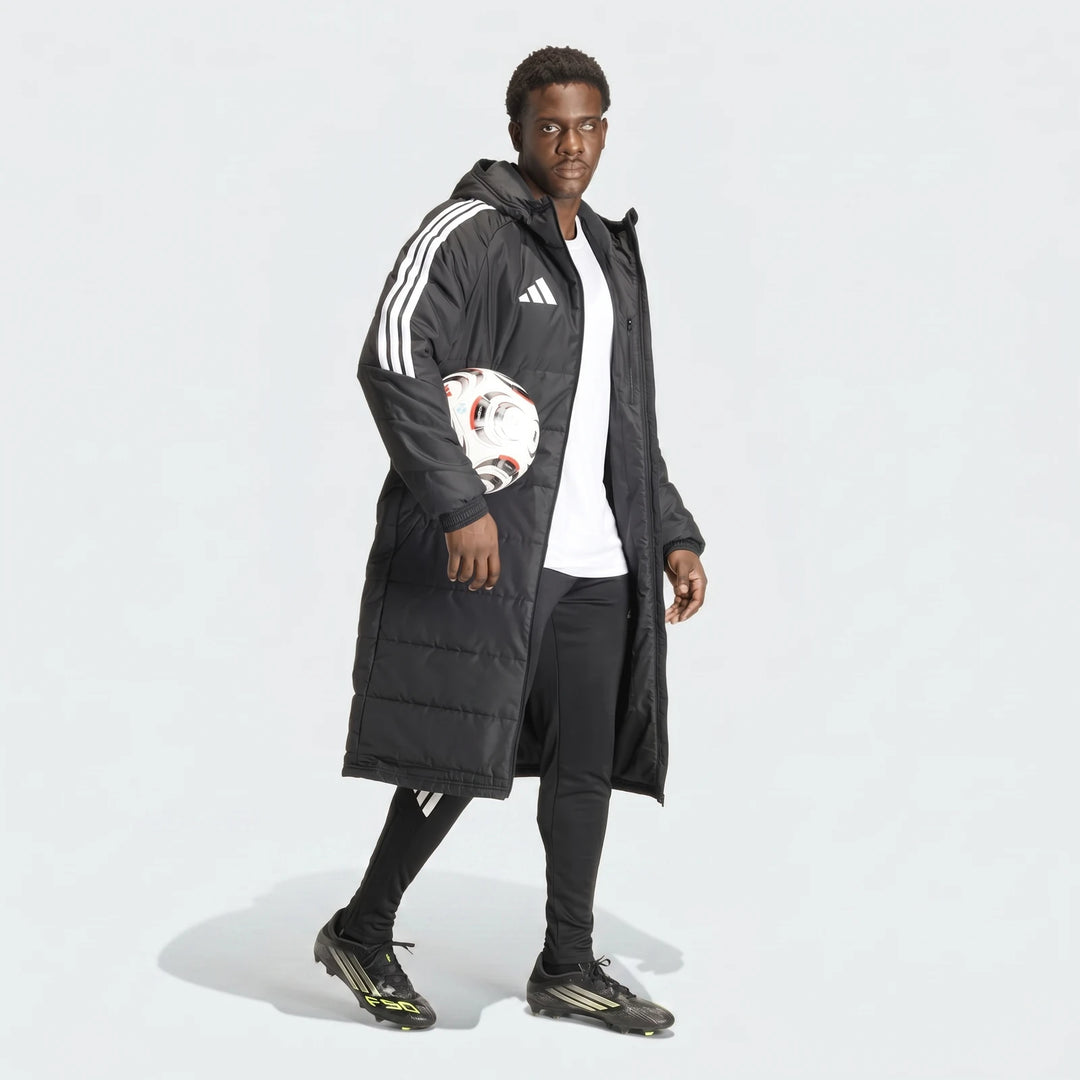 Black Adidas Tiro 26 Long Coat worn by a man, styled with black pants, soccer cleats, and holding a white soccer ball.