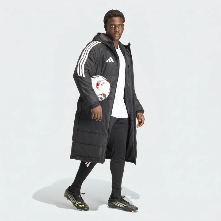 Black Adidas Tiro 26 Long Coat worn by a man, styled with black pants, soccer cleats, and holding a white soccer ball.
