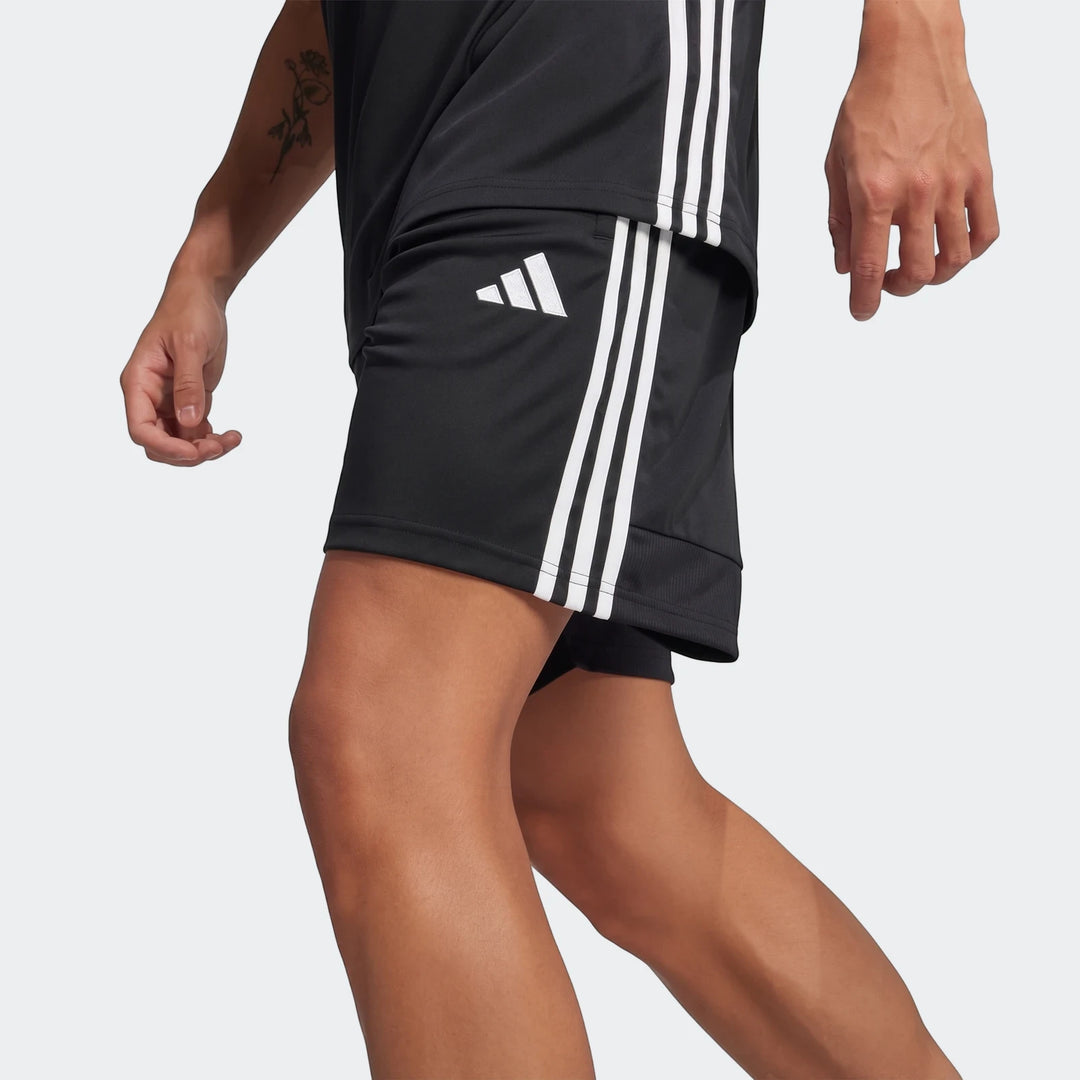 Close-up of black Adidas Tiro Essentials men's shorts with white stripes, worn by a model in a dynamic pose.