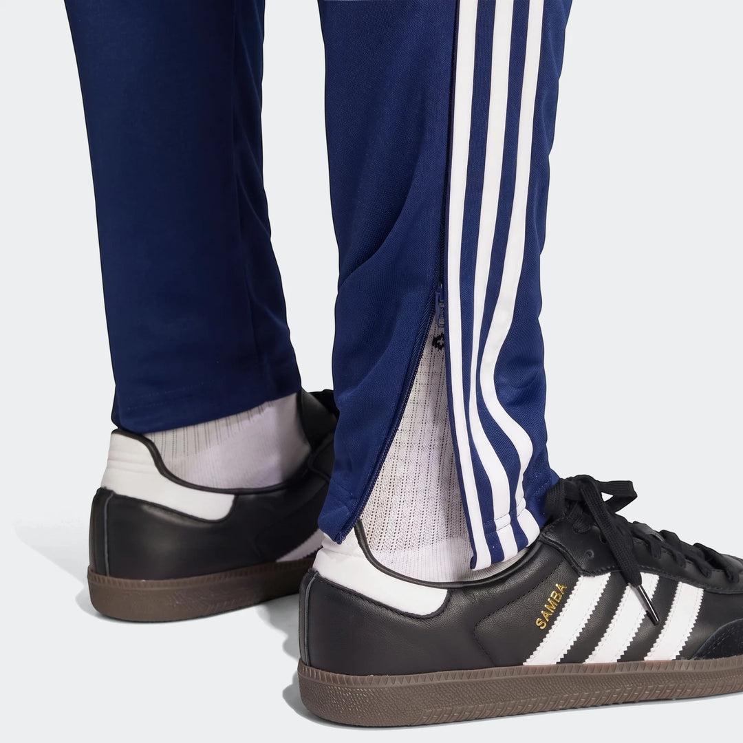 Navy blue Adidas Tiro Essentials Pants with white stripes and side zippers, paired with black and white Adidas Samba