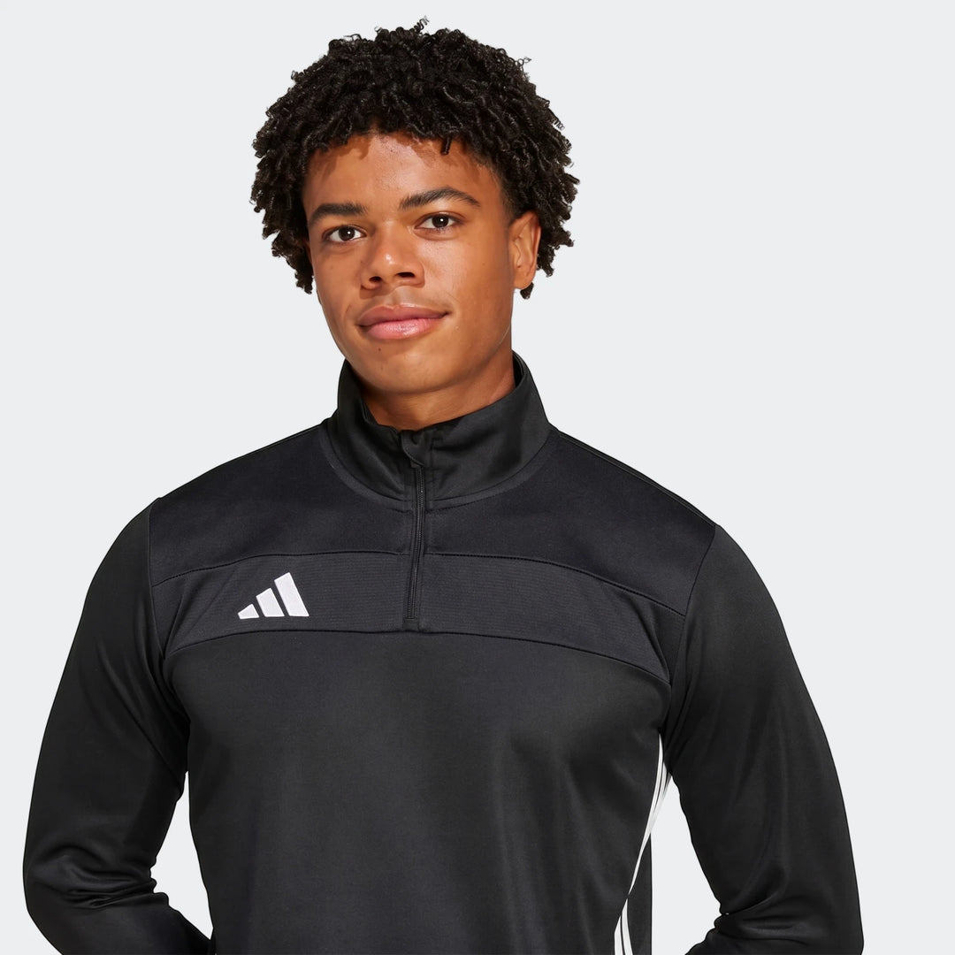 Young man wearing a black Adidas Tiro Essentials quarter-zip track top with white logo and side stripes in a studio shot.