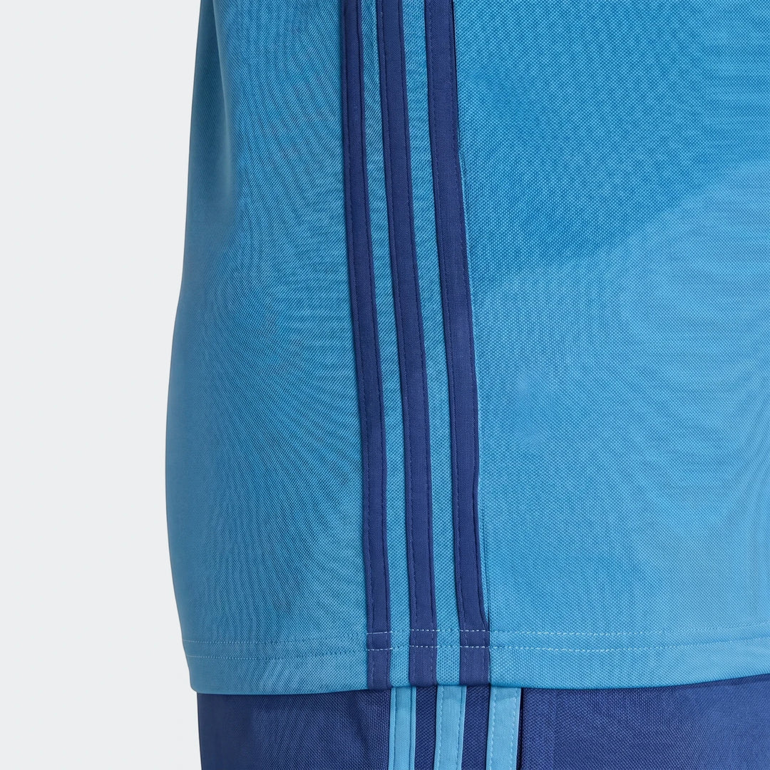 Close-up of a men's blue Adidas Tiro Essentials Track Top, featuring three dark blue stripes on the side and pique fabric.