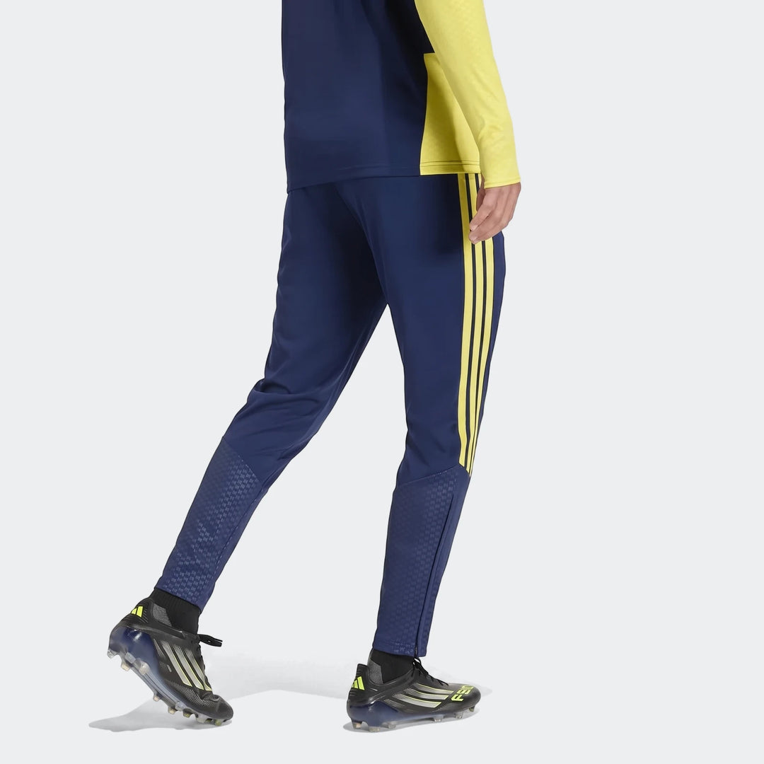Blue Adidas Tiro26 C track pants worn by a model, featuring yellow stripes and textured lower leg panels, captured in a