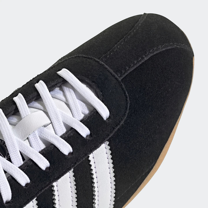 Close-up of black suede Adidas Tokyo Shoes with white laces and iconic white three stripes, showcasing the toe box and