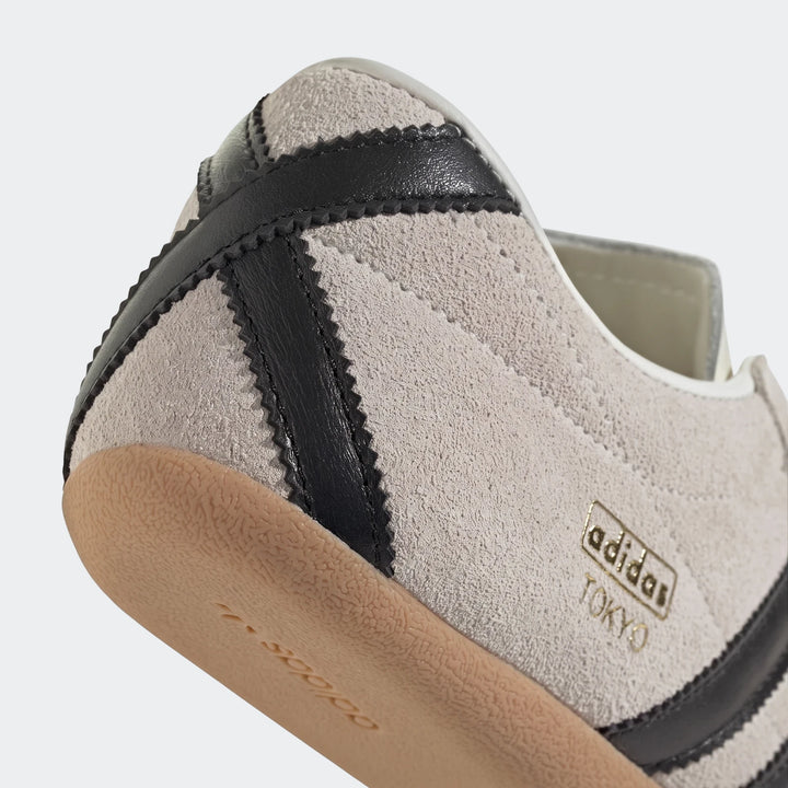 Close-up view of an Adidas Tokyo shoe in grey suede with black stripes and a light brown gum sole, showing the heel and side.