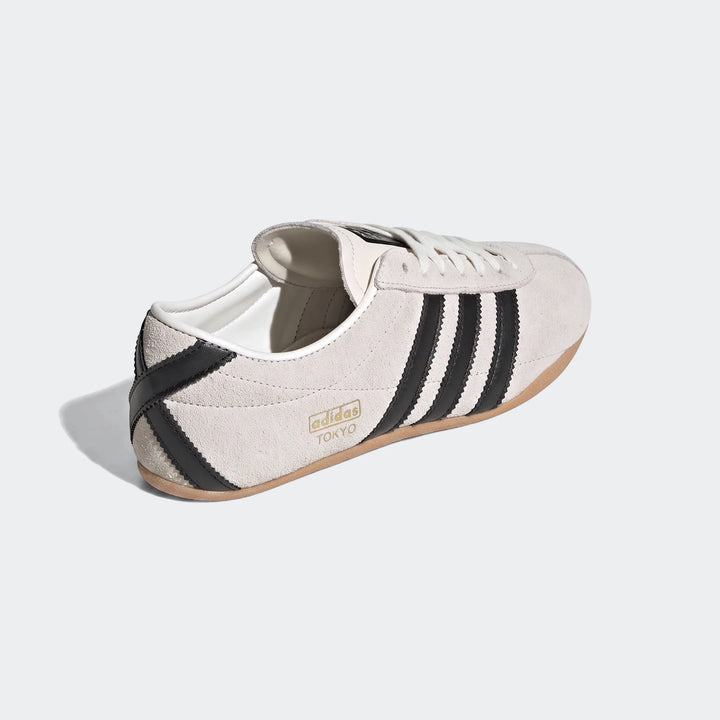 Angled side view of an off-white Adidas Tokyo suede shoe with black stripes and gum sole, featuring white laces.