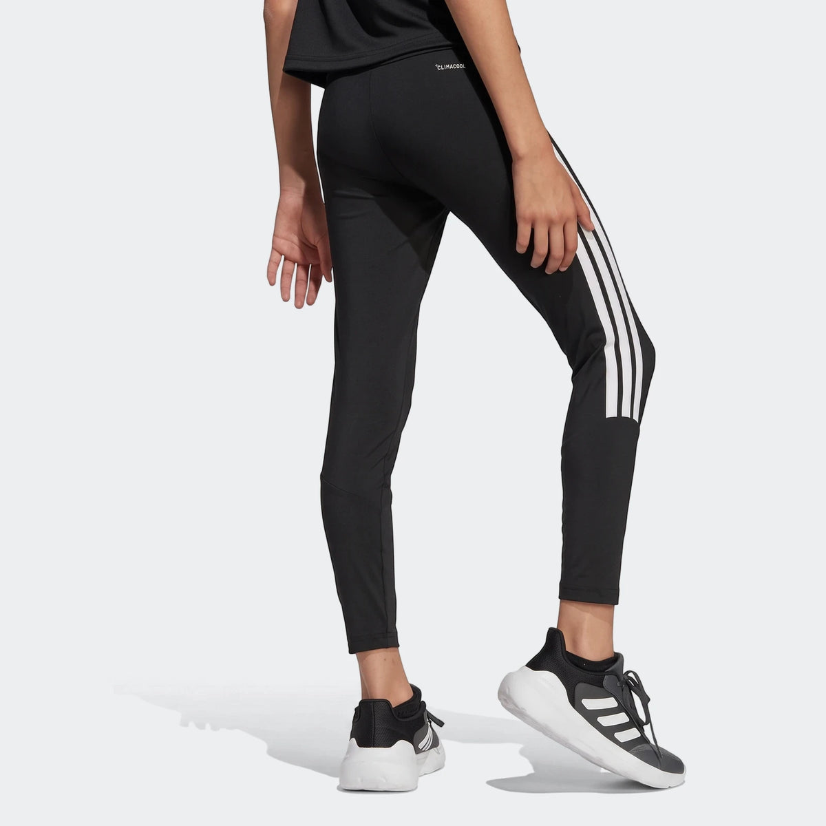 Black Adidas Train Essentials 3-Stripes Kids Leggings, featuring iconic white stripes, worn with black and white sneakers.