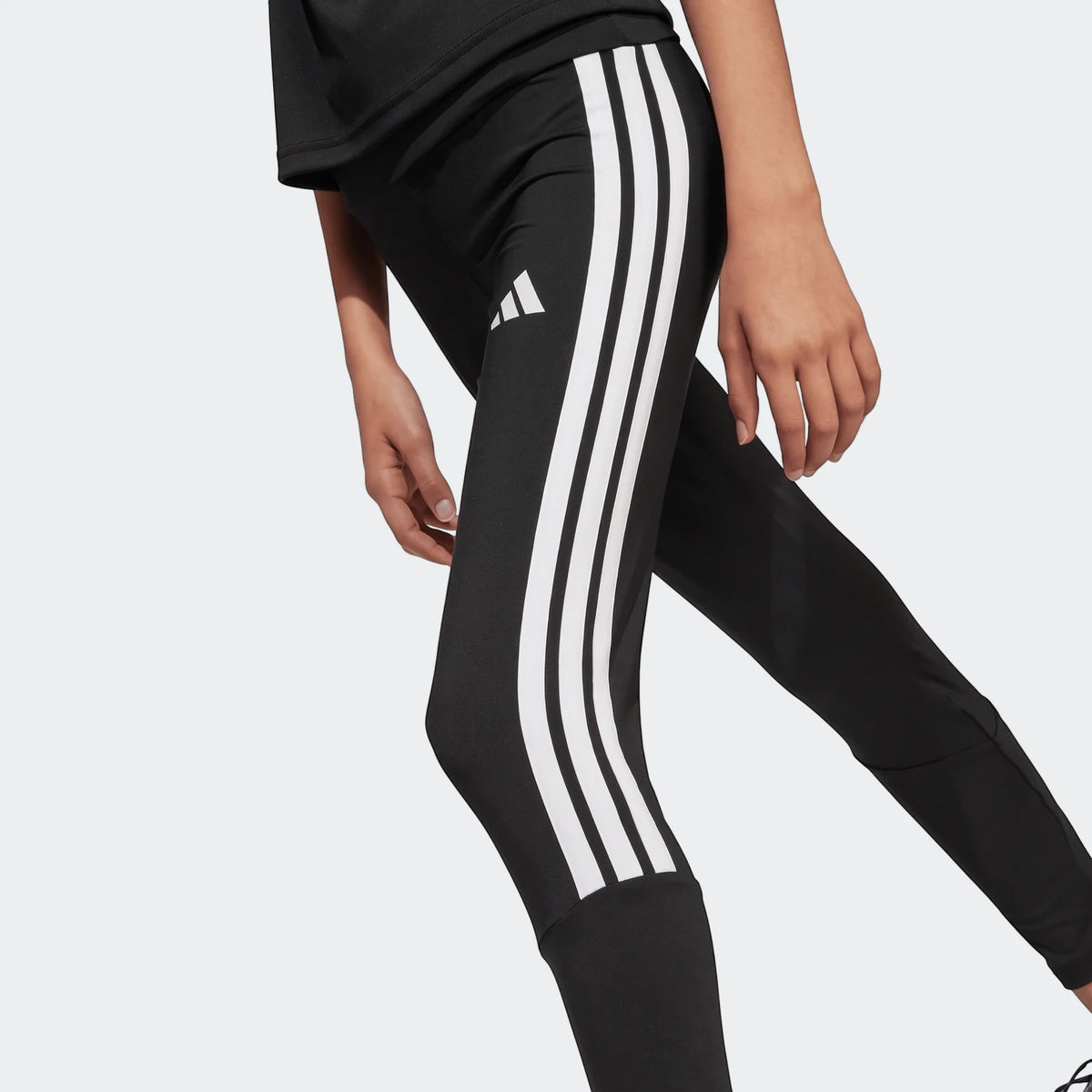 Close-up of a child wearing black Adidas Train Essentials 3-Stripes Leggings with white stripes, designed for active kids.