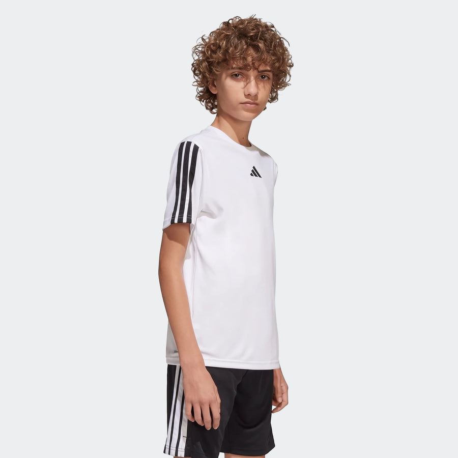 Young boy wearing a white Adidas Train Essentials 3-Stripes T-Shirt and black athletic shorts with white stripes.