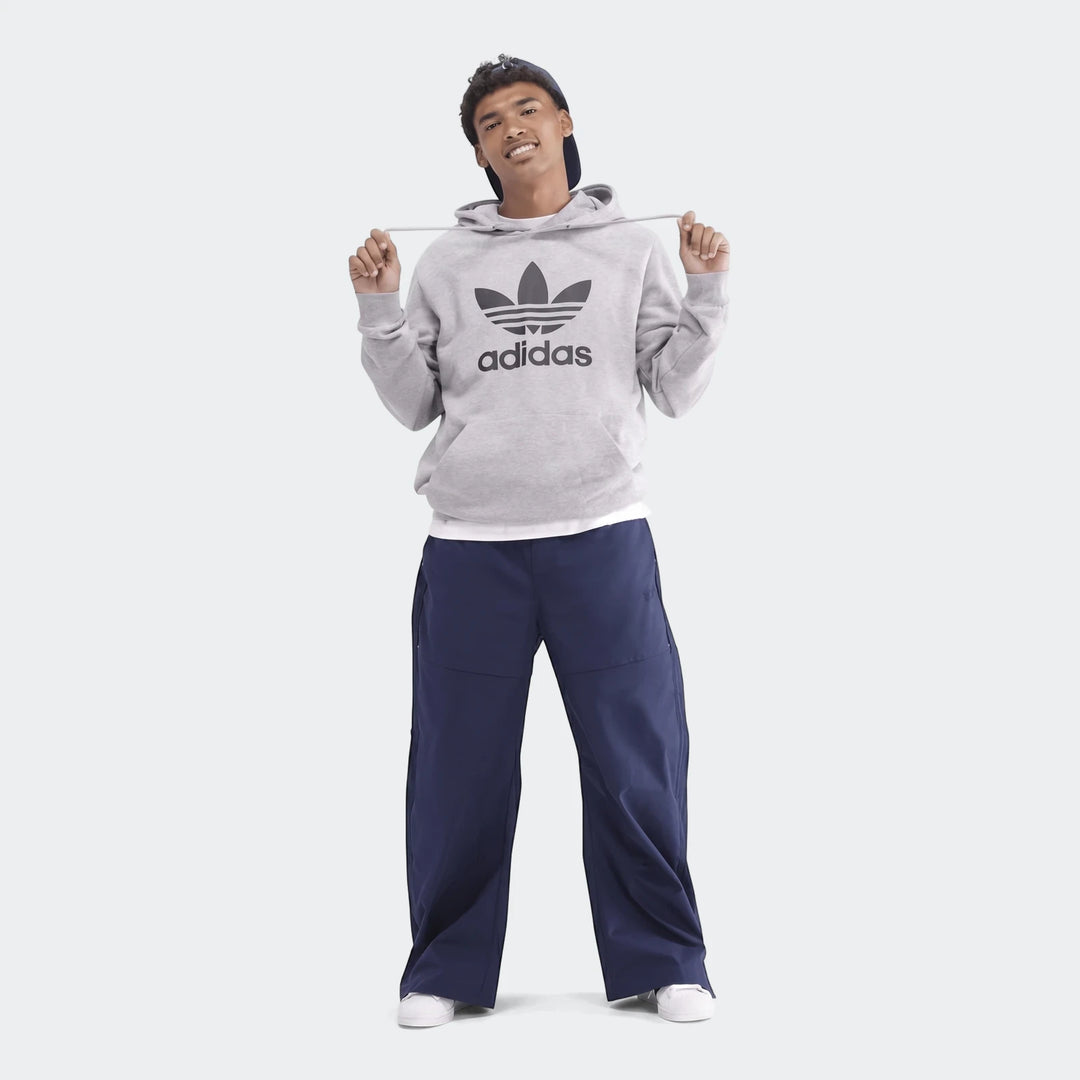 Young man models a grey Adidas Trefoil hoodie and navy wide-leg pants, standing full-body against a plain background. Adidas