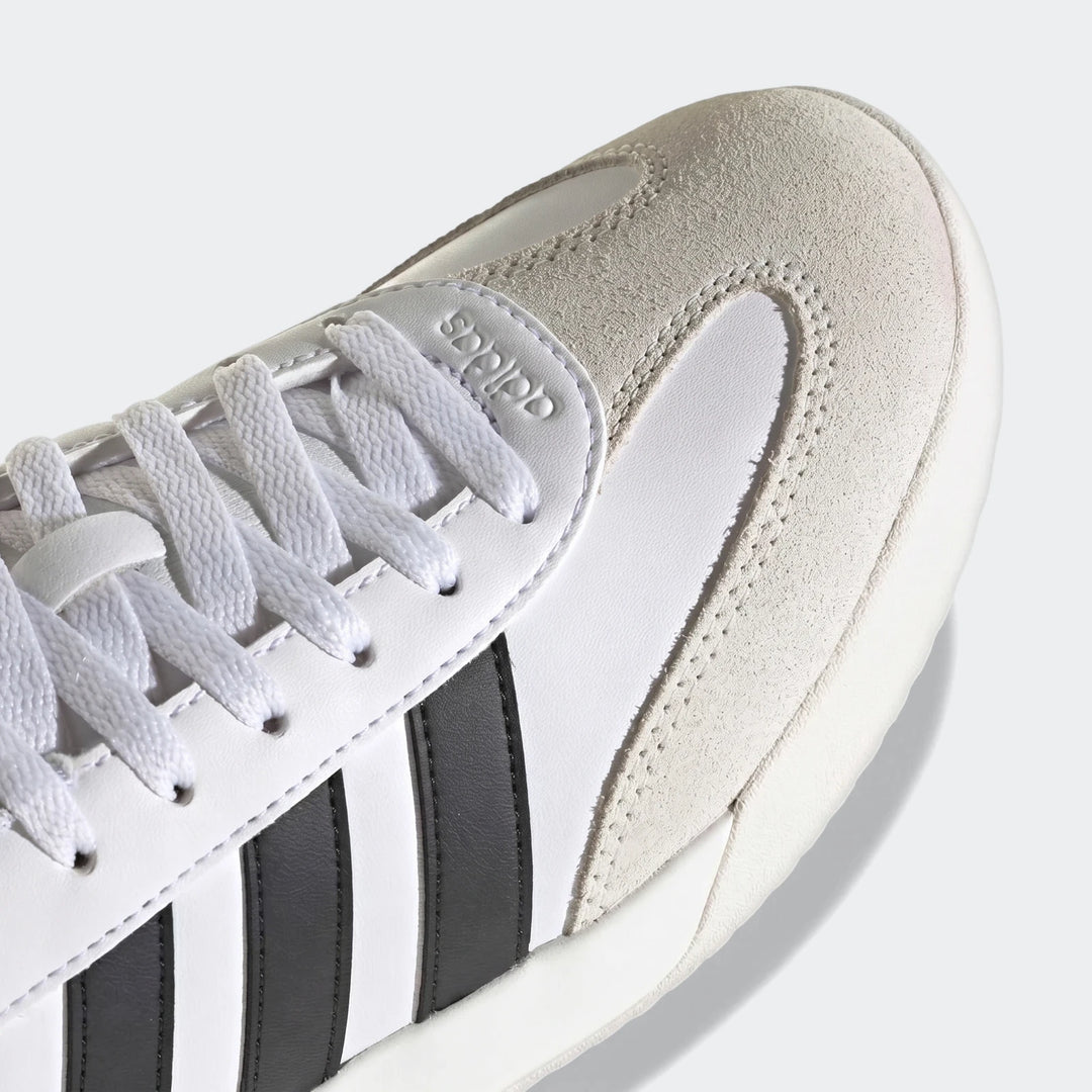 Close-up of white Adidas Vl Court sneakers with black stripes, featuring suede and synthetic leather details, from an
