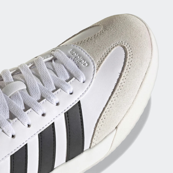 Close-up of white Adidas Vl Court sneakers with black stripes, featuring suede and synthetic leather details, from an