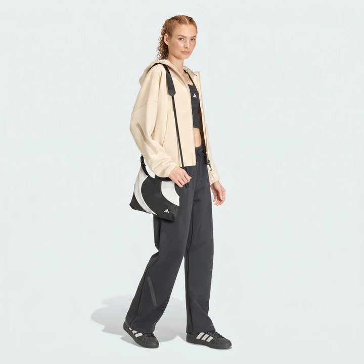 Woman in beige Adidas W Z.N.E. FZ jacket, black sports bra, and dark grey wide-leg pants with black sneakers and a graphic