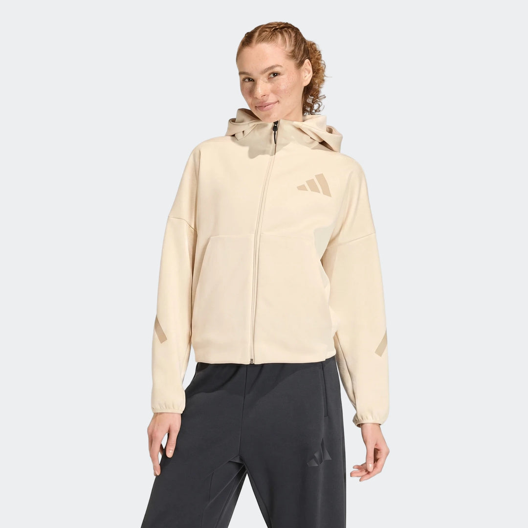 Woman wearing a beige Adidas W Z.N.E Fz full-zip hoodie and dark sweatpants, front view.