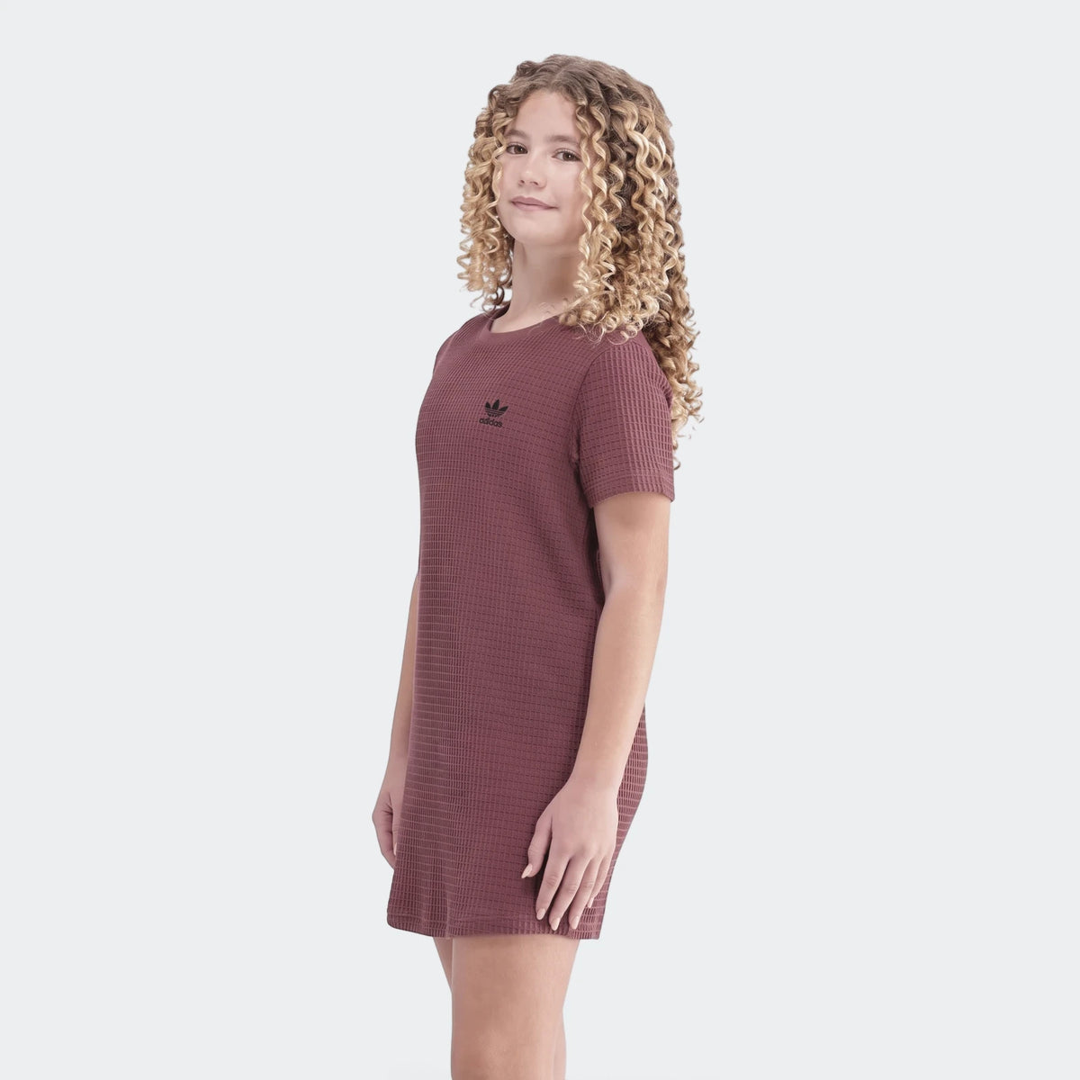 Full body shot of a young girl wearing a maroon short-sleeve Adidas Waffle Dress, showcasing its texture.