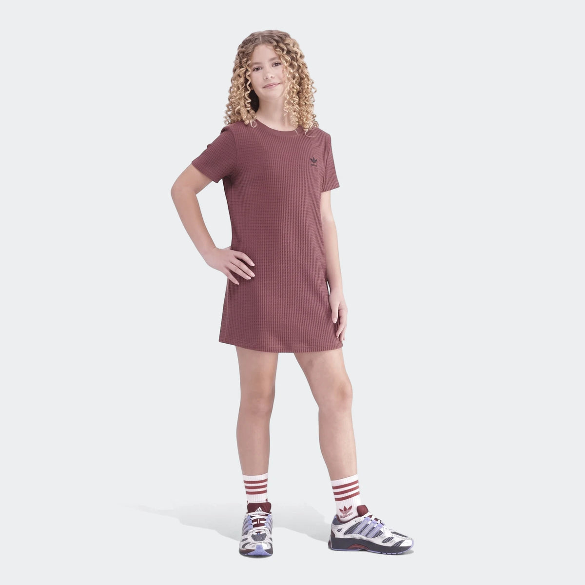 Full body shot of a young girl wearing a maroon Adidas Waffle Dress with waffle texture and striped socks, standing.