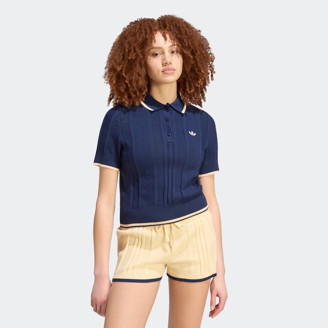 A model wears an Adidas navy blue Cable Knit Cali Tee Polo with cream and yellow trim, paired with matching knitted shorts.