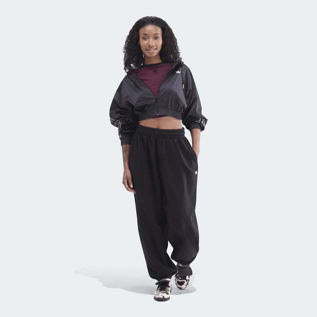 A woman wearing black Adidas Essentials French Terry Jogger Pants and a black cropped jacket with black and white sneakers.