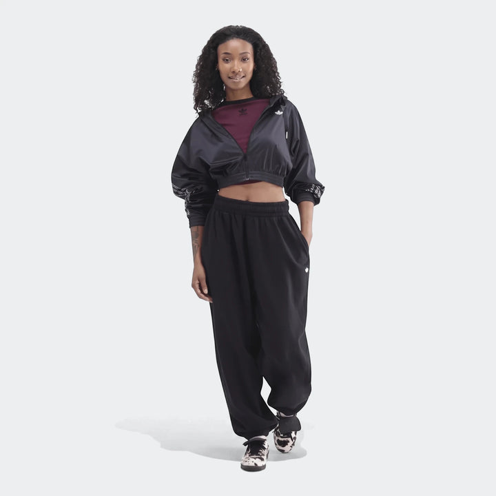 A woman wearing black Adidas Essentials French Terry Jogger Pants and a black cropped jacket with black and white sneakers.