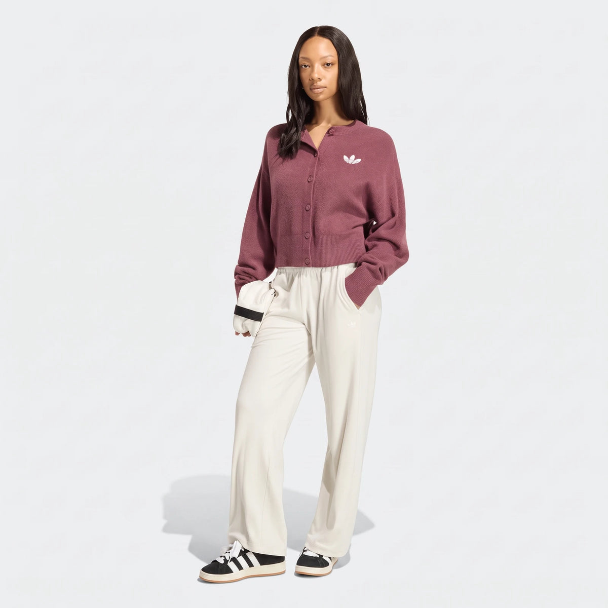 A woman models a maroon Adidas Essentials Knit Cardigan, cream wide-leg pants, and black Adidas sneakers, full body view.