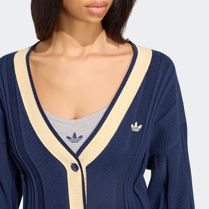 Close-up of a woman wearing a navy and cream Adidas V-neck Cable Knit Cardigan over a grey t-shirt, showcasing the knit