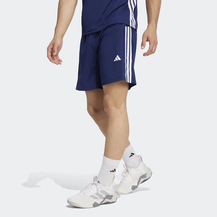 Male model in navy blue Adidas Workout Essentials Base 3-Stripes Woven Shorts, matching t-shirt, and white sneakers, posed