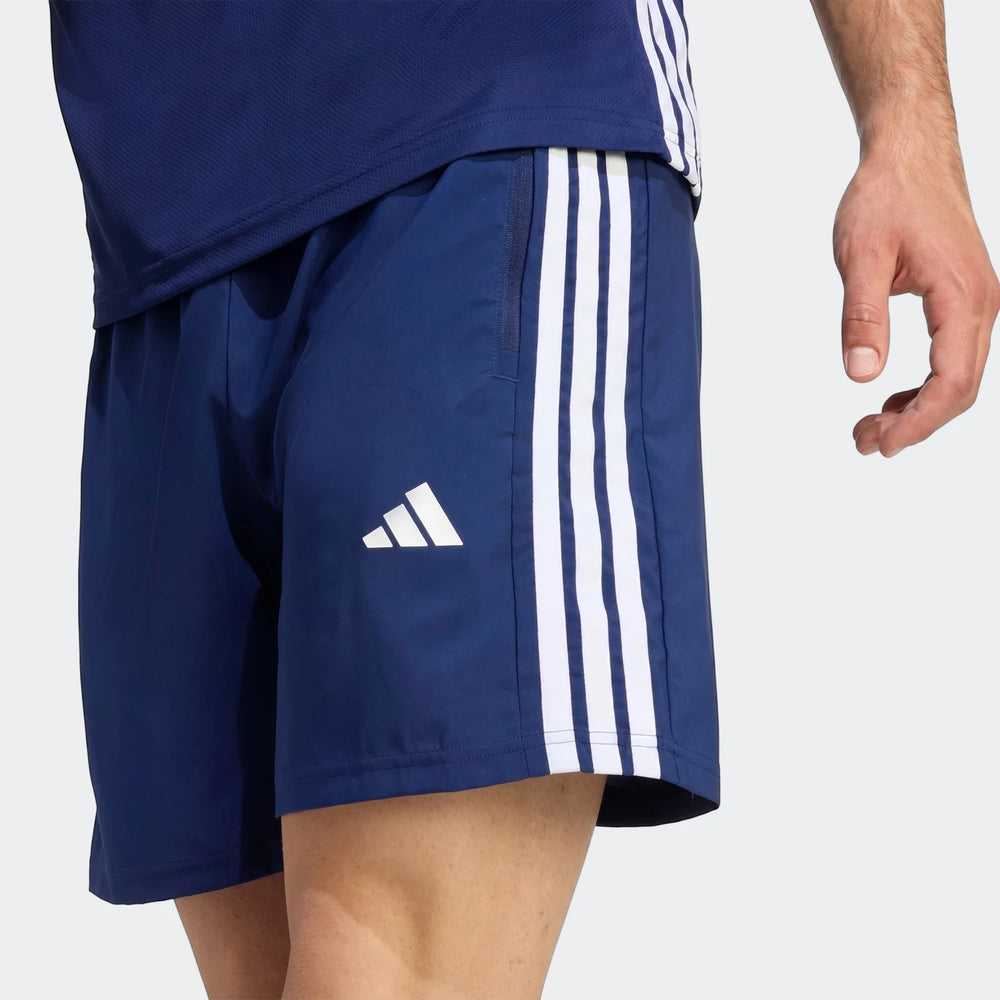 Close-up of blue Adidas Workout Essentials Base 3-Stripes Woven Shorts, featuring white stripes and logo, worn by a male