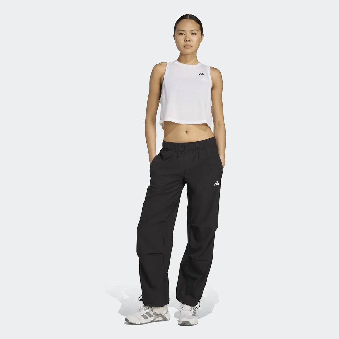 Full body shot of a woman wearing black Adidas Workout Essentials Woven Training Joggers and a white crop top, standing.
