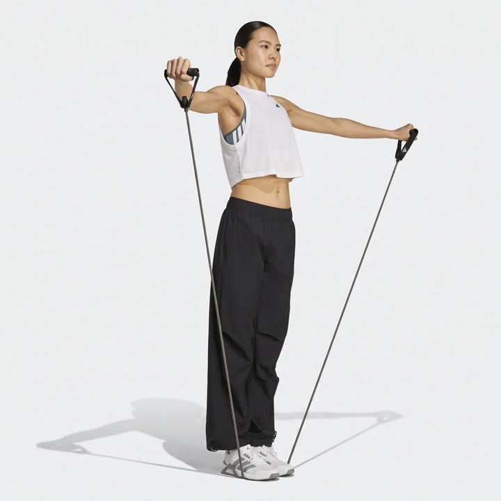 Woman wearing black Adidas Workout Essentials Woven Training Joggers and a white crop top, exercising with a resistance band.