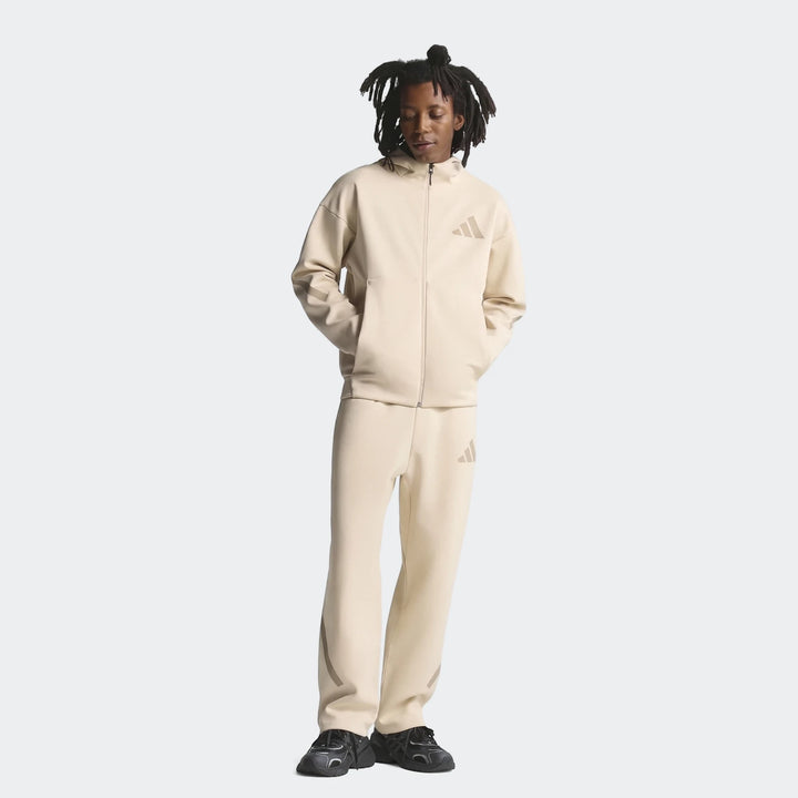 Male model wearing a beige Adidas Z.N.E. full-zip tracksuit with matching pants, standing front view.