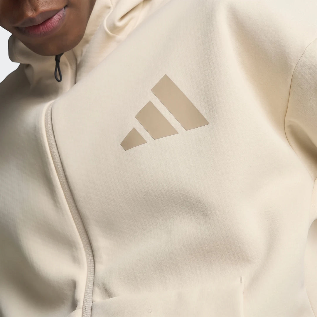 Close-up of a cream Adidas Z.N.E. Full-Zip Hoodie on a model, featuring the iconic three-bar logo and front zipper.