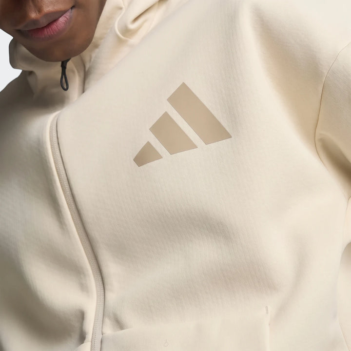 Close-up of a cream Adidas Z.N.E. Full-Zip Hoodie on a model, featuring the iconic three-bar logo and front zipper.
